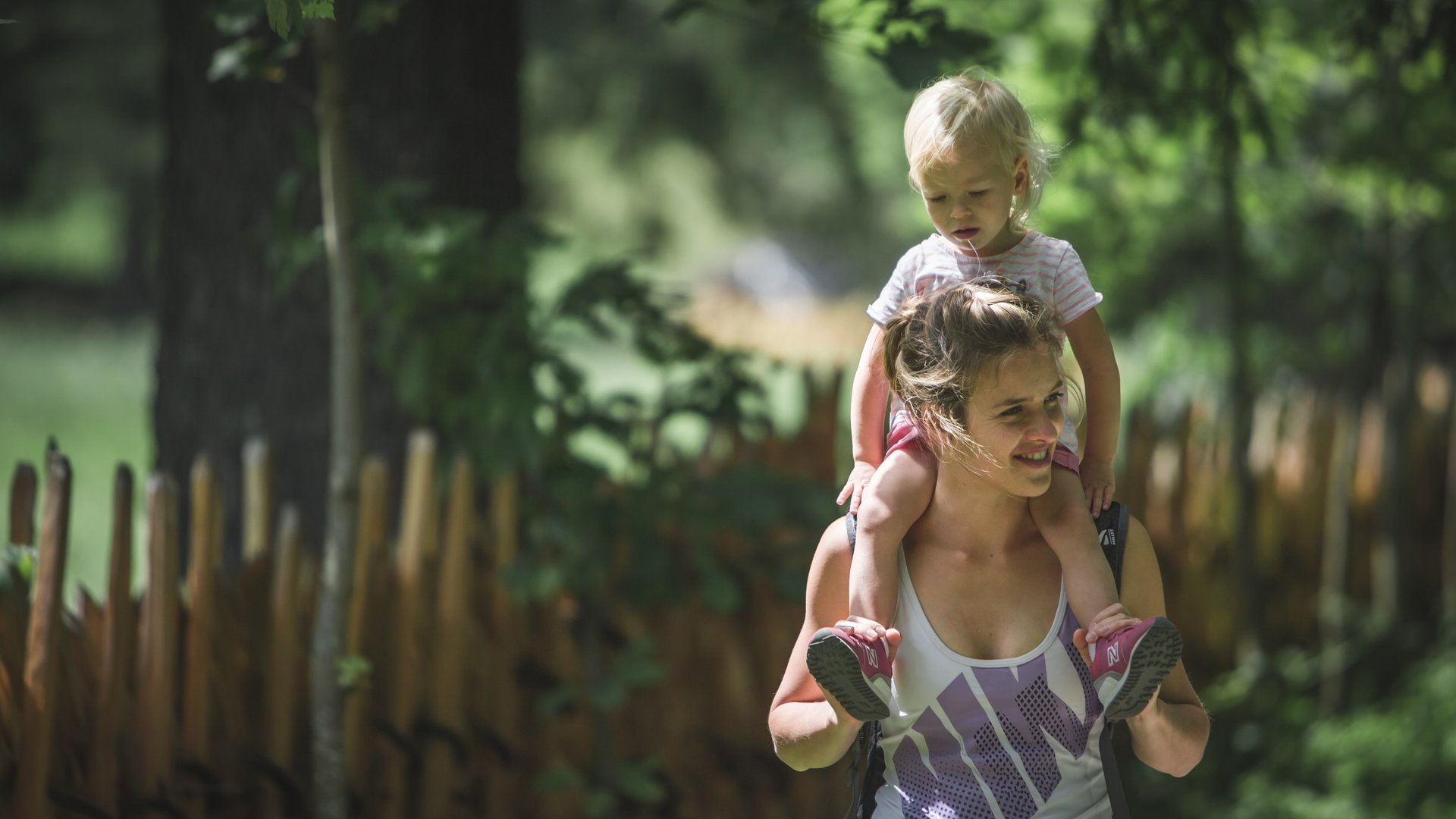 Unterkunft bei Ladurns für Familien Frau trägt Kind auf Schultern im Wald bei Sonnenschein