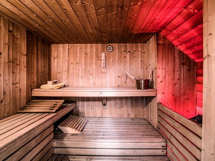 Entdecker- und Wellnesshotel in Sterzing Holzsauna mit roter Beleuchtung, Aufgusskübel und Handtüchern