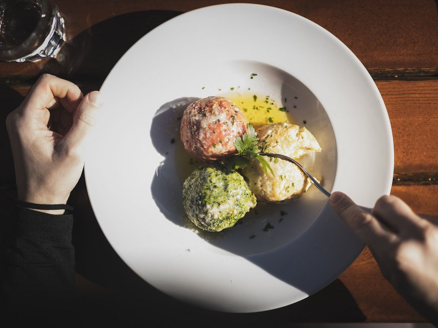 Das Skigebiet Ladurns und andere Winter-Highlights Drei bunte Klöße auf weißem Teller mit Besteck und Glas Wasser
