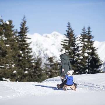 Gudruns Blog: alles über Sterzing, übers Wandern, über Tirol Frau zieht Kind auf Schlitten durch verschneite Winterlandschaft mit Tannen