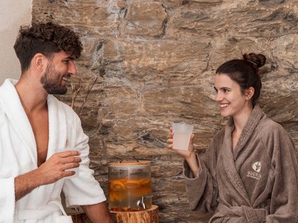 Entdecker- und Wellnesshotel in Sterzing Mann und Frau trinken Wasser in Bademänteln vor steinerner Wand