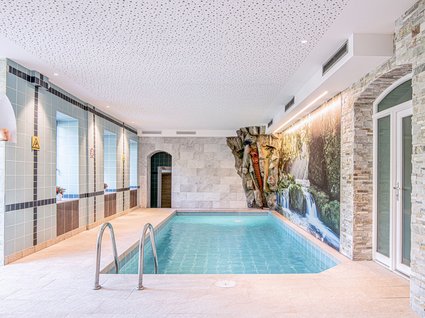 Entdecker- und Wellnesshotel in Sterzing Innenpool mit Wasserfallwand und modernen Fliesenwänden