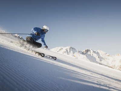 Gudrun Gossensass: Wandern, Radfahren und vieles mehr Skifahrer fährt auf präparierter Piste mit verschneiten Bergen im Hintergrund