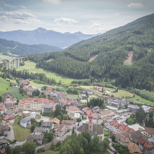 Hotel in Gossensass: welcome to Gudrun! Luftaufnahme eines Dorfes in einem grünen Tal mit Bergen und einer Autobahnbrücke