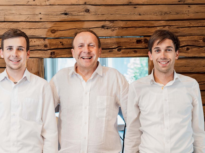 Eines der coolsten Hotels in Gossensass (Südtirol) Drei lächelnde Männer in weißen Hemden vor Holzwand