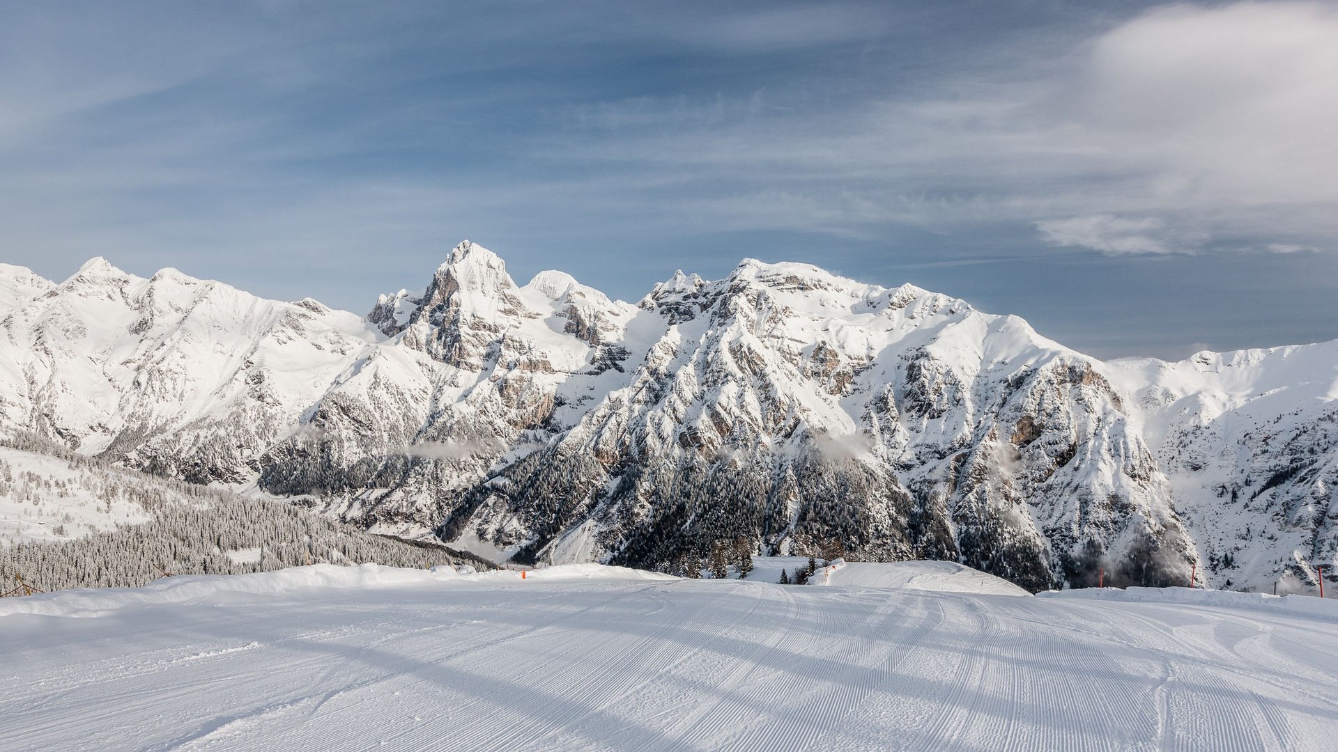 Das Skigebiet Ladurns und andere Winter-Highlights Frisch präparierte Skipiste vor schneebedeckten Bergen unter blauem Himmel