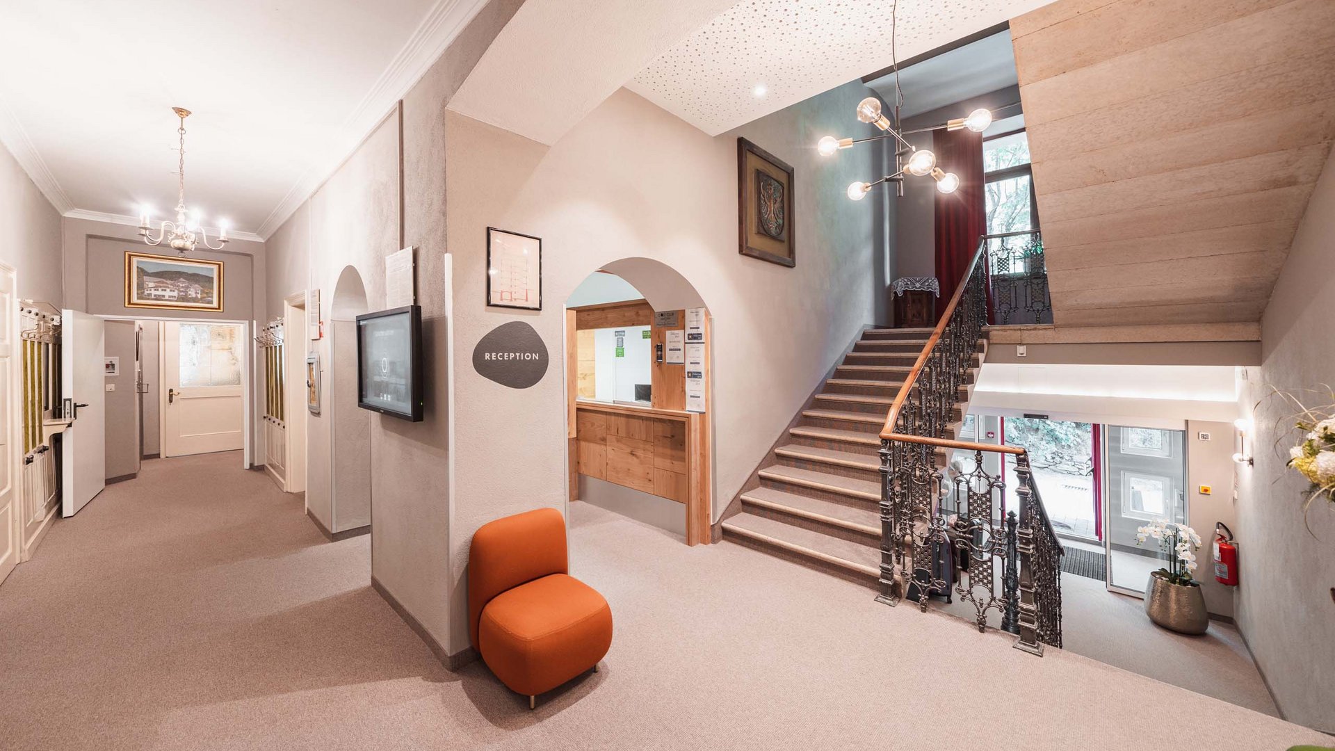 Eines der coolsten Hotels in Gossensass (Südtirol) Helle Hotellobby mit Rezeption, Treppe und Sitzbereich mit orangenem Stuhl