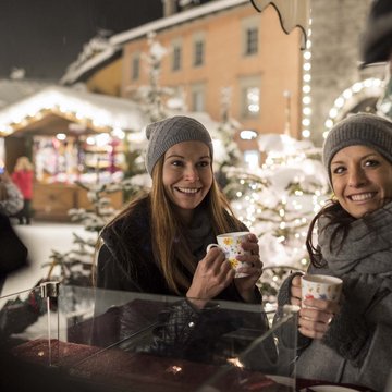 Gudruns Blog: alles über Sterzing, übers Wandern, über Tirol Lächelnde Freunde trinken Heißgetränke auf einem winterlichen Weihnachtsmarkt