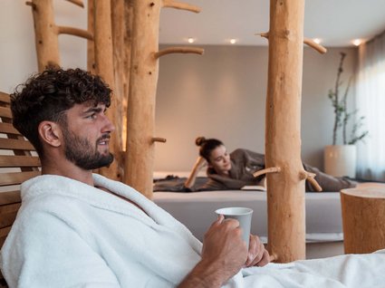 Entdecker- und Wellnesshotel in Sterzing Mann in weißem Bademantel mit Tasse, Frau entspannt im Hintergrund