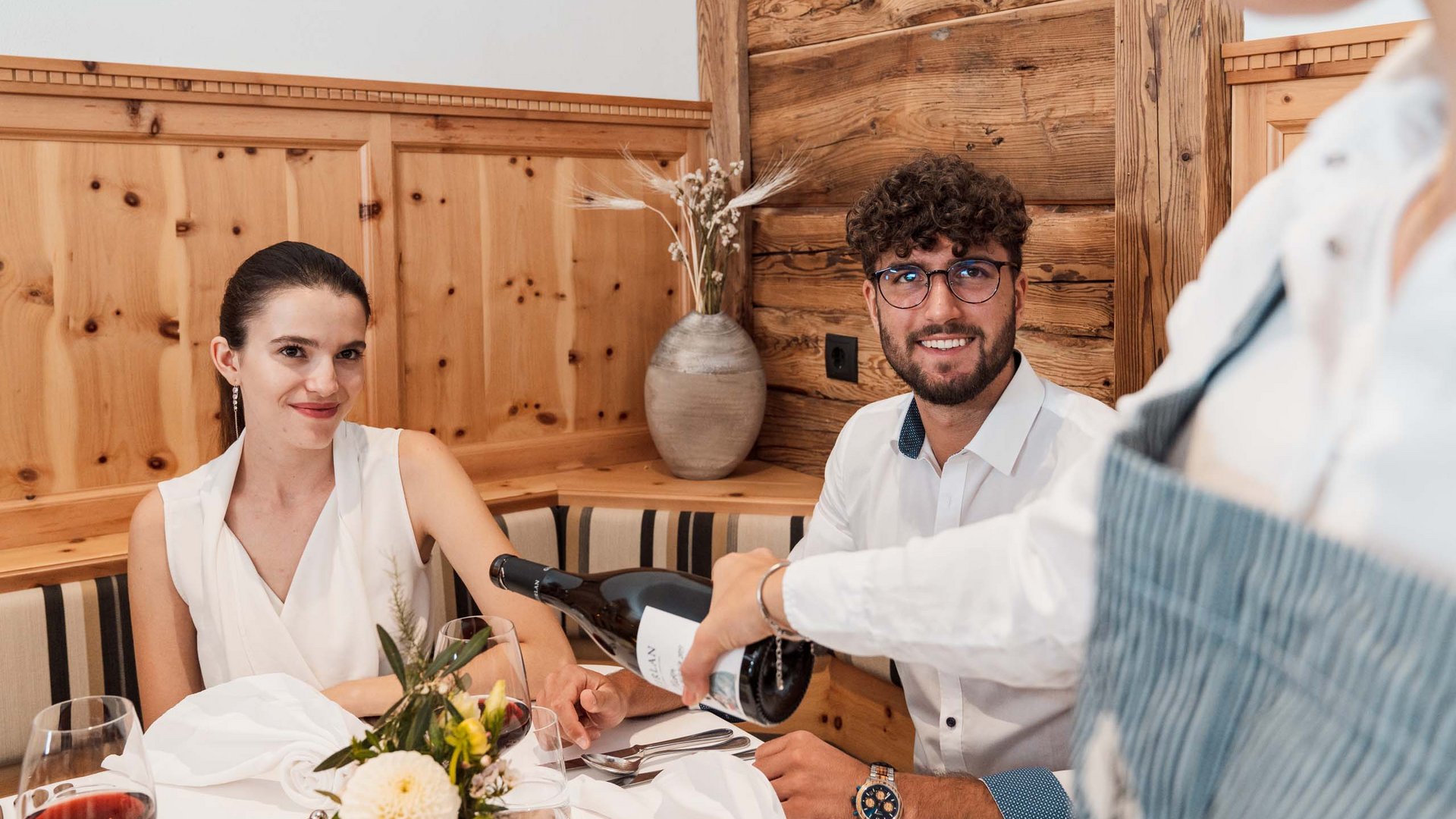 Eines der coolsten Hotels in Gossensass (Südtirol) Paar sitzt im Restaurant, Kellner schenkt Wein am Tisch ein