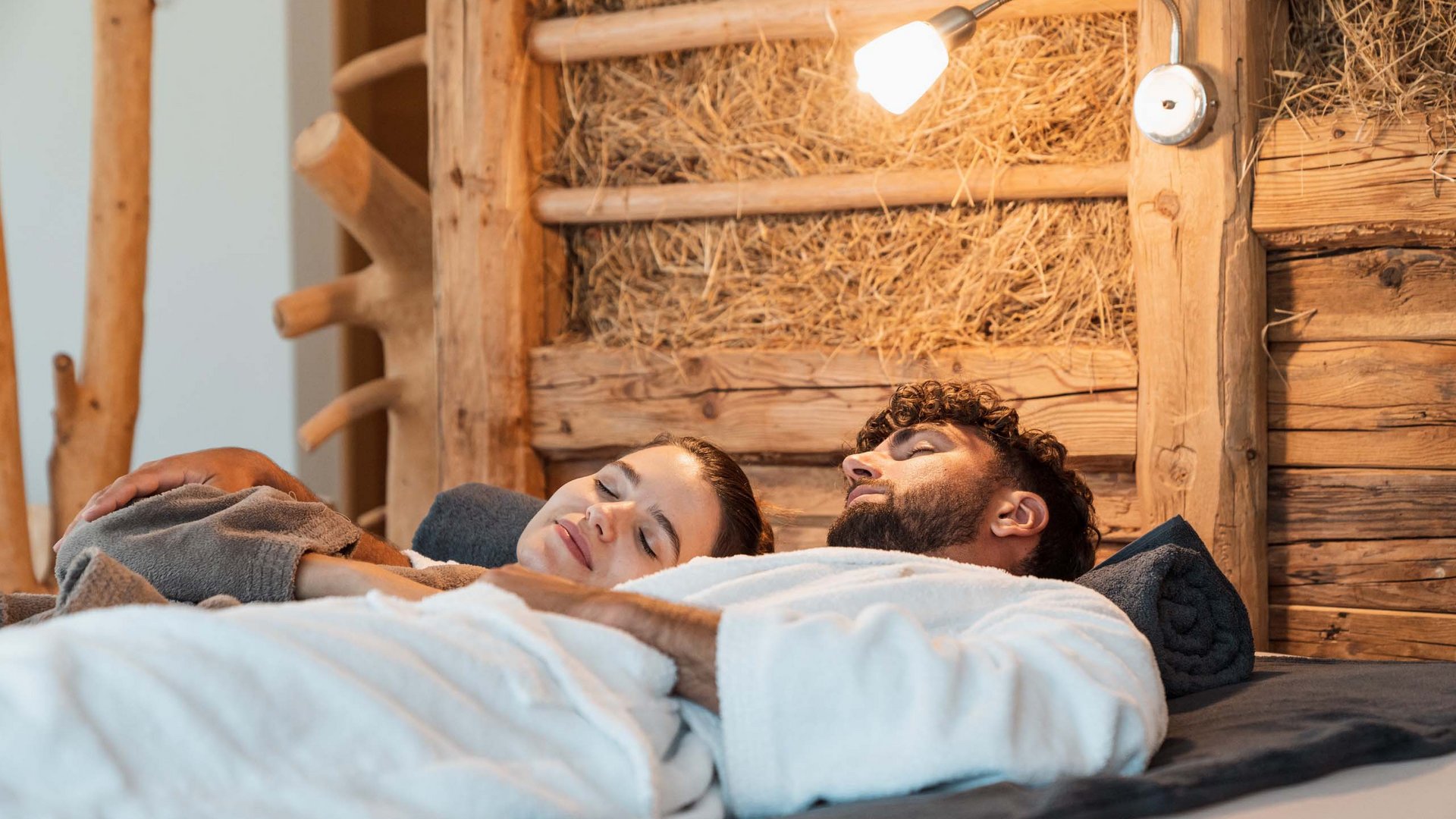 Entdecker- und Wellnesshotel in Sterzing Entspanntes Paar in Bademänteln liegend im rustikalen Zimmer