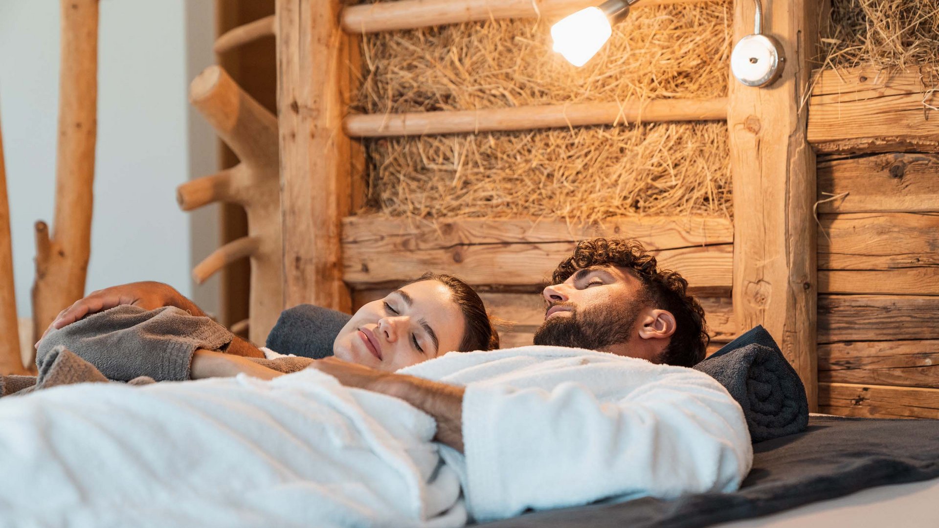 Eines der coolsten Hotels in Gossensass (Südtirol) Entspanntes Paar in Bademänteln liegend im rustikalen Zimmer