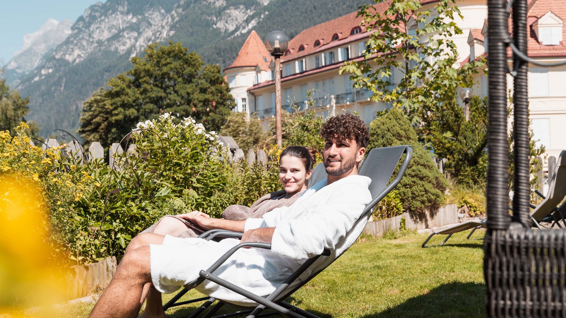 Eines der coolsten Hotels in Gossensass (Südtirol) Paar entspannt im Garten eines Hotels mit Bergblick an sonnigem Tag