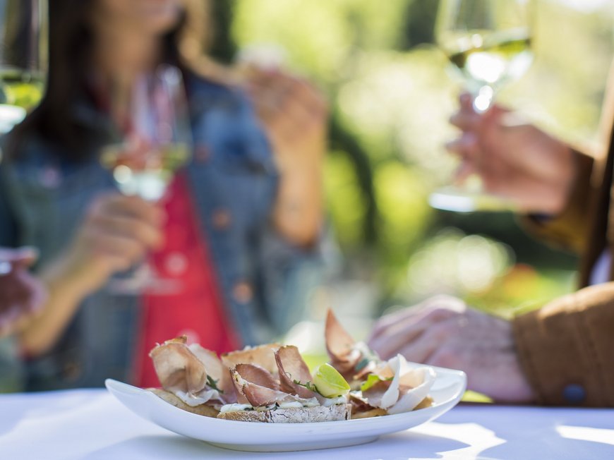 Hiking in Sterzing and the surrounding area Plate of appetizers with meat and people holding wine glasses in the background