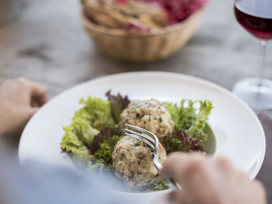 Hiking in Sterzing and the surrounding area Person eating two dumplings on lettuce with glass of red wine and bread basket