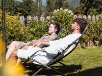 Gudrun in Gossensass: Hotel mit Herz Paar entspannt sich in Bademänteln draußen auf Liegestühlen im Garten