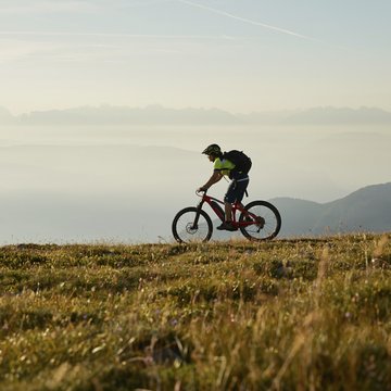 Gudrun in Gossensass: Hotel mit Herz Mountainbiker fährt auf einem Berg mit Nebel und Bergen im Hintergrund