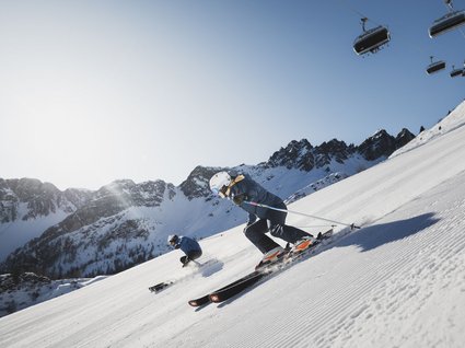 Gudrun in Gossensass: Hotel mit Herz Zwei Skifahrer auf präparierter Piste unter blauem Himmel in den Bergen